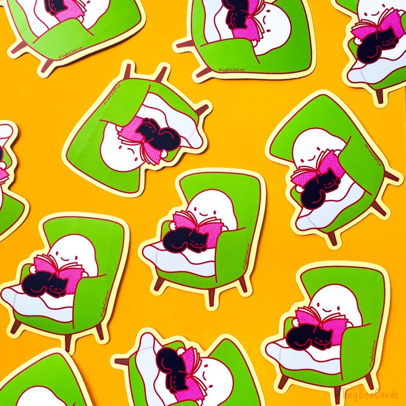 May include: A set of nine stickers featuring a ghost reading a book in a green armchair with a black cat curled up on its lap. The stickers are on a yellow background.