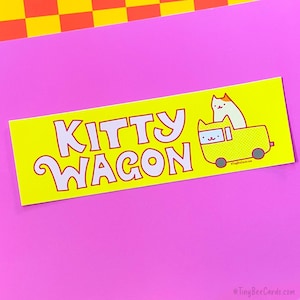 May include: A yellow sticker with the words "KITTY WAGON" in white, outlined in red. A cartoon cat is in a yellow wagon. The background is pink and yellow.