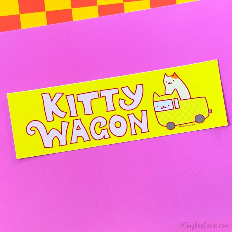 Pode incluir: Um adesivo amarelo com as palavras "KITTY WAGON" em branco, contornadas em vermelho. Um gato de desenho animado est&aacute; em uma carro&ccedil;a amarela. O fundo &eacute; rosa e amarelo.