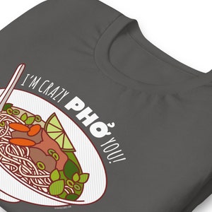 Op de afbeelding: Een donkergrijs T-shirt met een witte kom pho en de tekst "I'm crazy pho you!" erop gedrukt.
