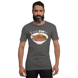 Op de afbeelding: Een donkergrijs T-shirt met een witte afbeelding van een kom pho met de tekst "I'm crazy pho you!"