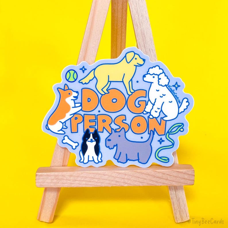 May include: A blue and yellow sticker with the text "Dog Person" and illustrations of five dogs. The dogs are a golden retriever, a poodle, a corgi, a black and white dog, and a grey terrier.