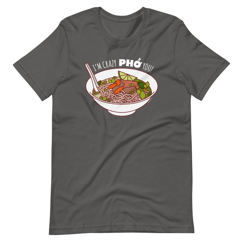 Op de afbeelding: Een donkergrijs T-shirt met een witte kom pho erop. De kom bevat noedels, vlees, groenten en een limoenwig. De tekst "I'm crazy PHO you!" is op het shirt gedrukt.
