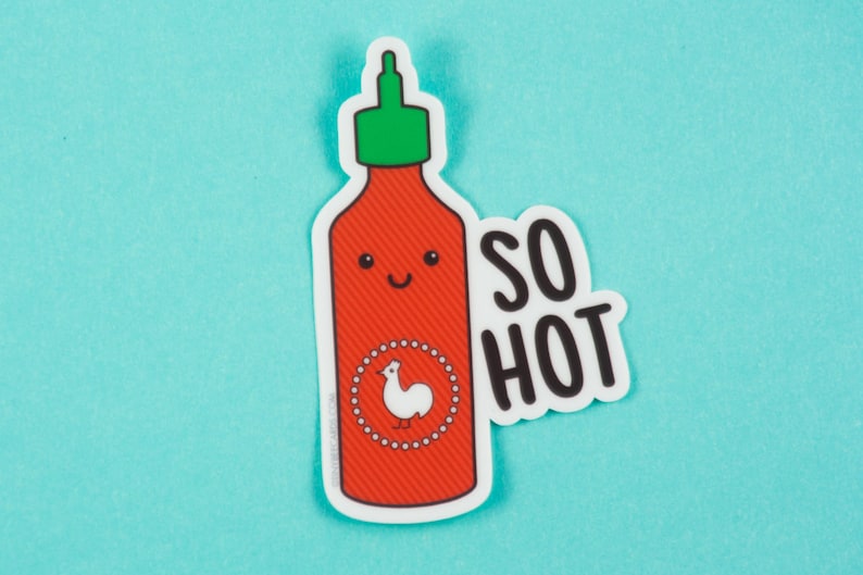 May include: A red and white hot sauce bottle with a green lid and a white rooster logo. The bottle has a smiling face and the text "SO HOT" is written in black on a white background.