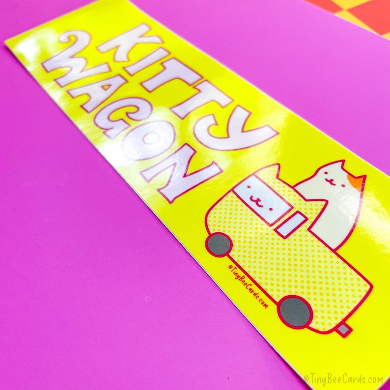 Pode incluir: Um autocolante amarelo com as palavras "KITTY WAGON" em letras brancas. O autocolante apresenta um gato de desenho animado a conduzir uma carrinha amarela com acabamentos vermelhos. A carrinha tem rodas cinzentas e o texto "TinyBeeCards.com" est&aacute; impresso na parte inferior.