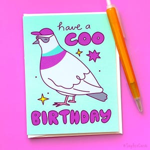 K&ouml;nnte beinhalten: Eine Gru&szlig;karte mit einer Cartoon-Illustration einer Taube, die eine Sonnenbrille und einen Hut tr&auml;gt. Die Karte hat einen hellblauen Hintergrund mit rosa und wei&szlig;en Akzenten. Der Text auf der Karte lautet "have a coo birthday".