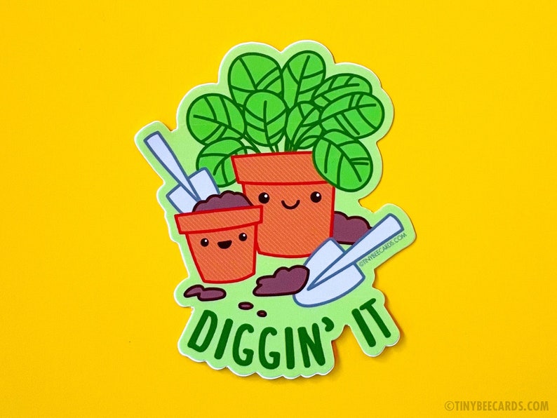 K&ouml;nnte beinhalten: Eine gr&uuml;ne Pflanze in einem Terrakotta-Topf mit einem fr&ouml;hlichen Gesicht, neben einem kleineren Topf mit einem fr&ouml;hlichen Gesicht und einer kleinen Schaufel. Der Text "Diggin' it" steht unter den T&ouml;pfen.