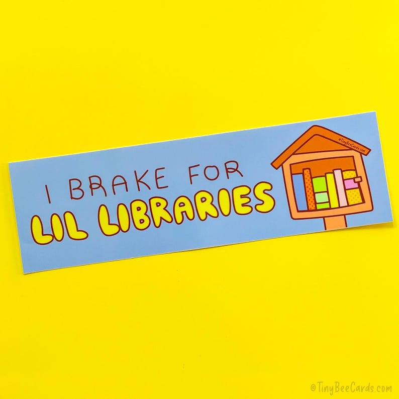 May include: A light blue bumper sticker with the text "I Brake for Lil Libraries" in brown and yellow. A cartoon illustration of a miniature library is on the right side of the sticker.