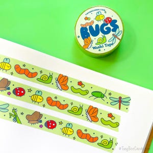 May include: A roll of green washi tape with a repeating pattern of colorful cartoon bugs, including a ladybug, a snail, a caterpillar, a butterfly, a bee, a dragonfly, and a praying mantis. The tape is packaged on a spool with a green background and the words "BUGS Washi Tape" in blue and white letters.