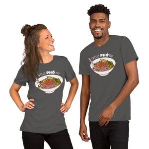 Op de afbeelding: Twee mensen dragen donkergrijze T-shirts met een witte afbeelding van een kom Pho en de tekst "I'm crazy Pho you!"