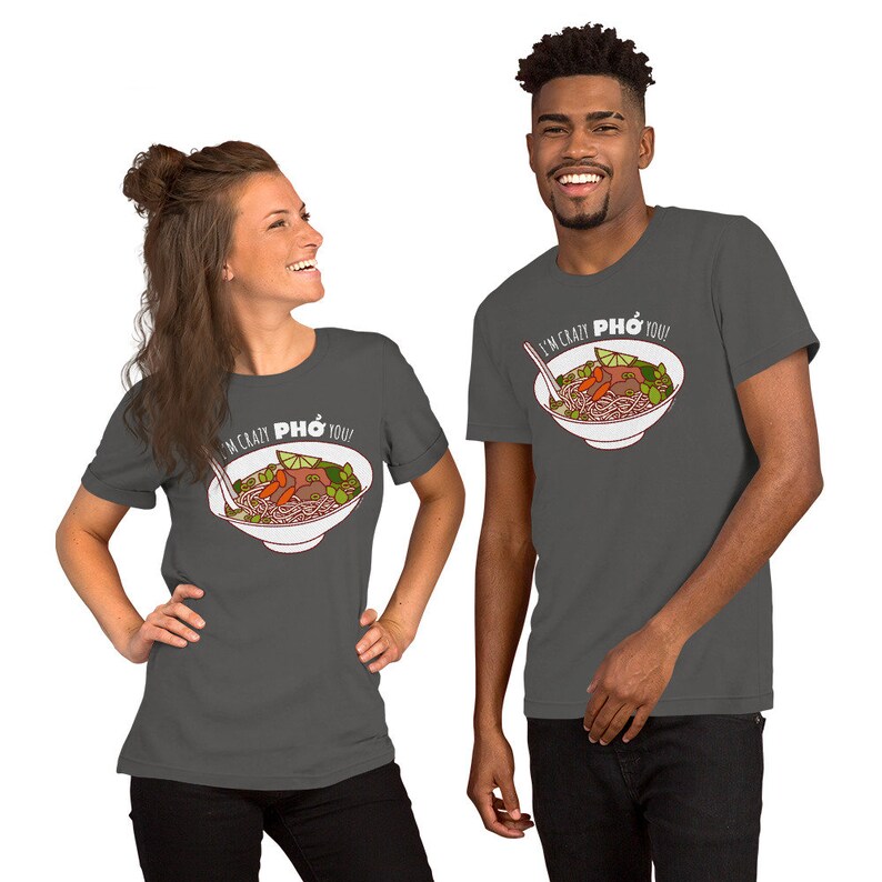 Op de afbeelding: Twee mensen dragen donkergrijze T-shirts met een witte afbeelding van een kom Pho en de tekst "I'm crazy Pho you!"