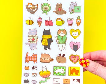 Può includere: Un foglio di adesivi impermeabili con varie illustrazioni a tema gatto. Gli adesivi raffigurano gatti in ciotole, con maglioni e in altre pose giocose. Il testo "cat life" e "Tiny Bee Cards" è stampato in alto.