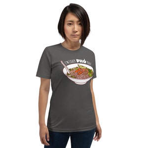 Op de afbeelding: Een donkergrijs T-shirt met een witte afbeelding van een kom pho met de tekst "I'm crazy pho you!" gedrukt op de voorkant.