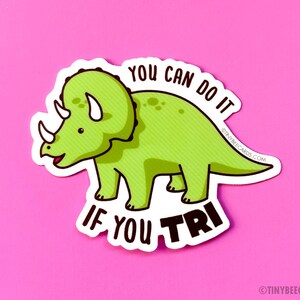 May include: Green cartoon triceratops dinosaur sticker with the text "You can do it if you tri" on a pink background.