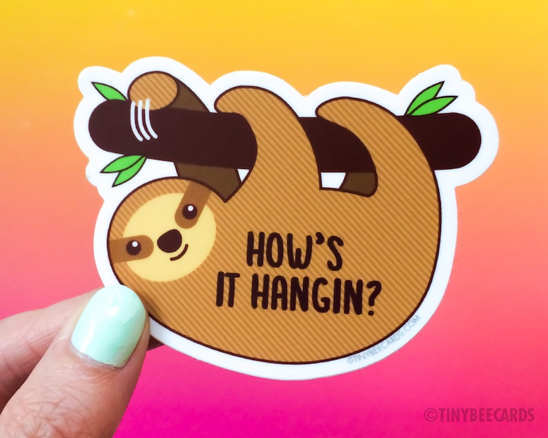May include: A brown sloth sticker with a white outline, hanging upside down from a branch. The sloth has a cute face and the text "How's it hangin?" is written below it.