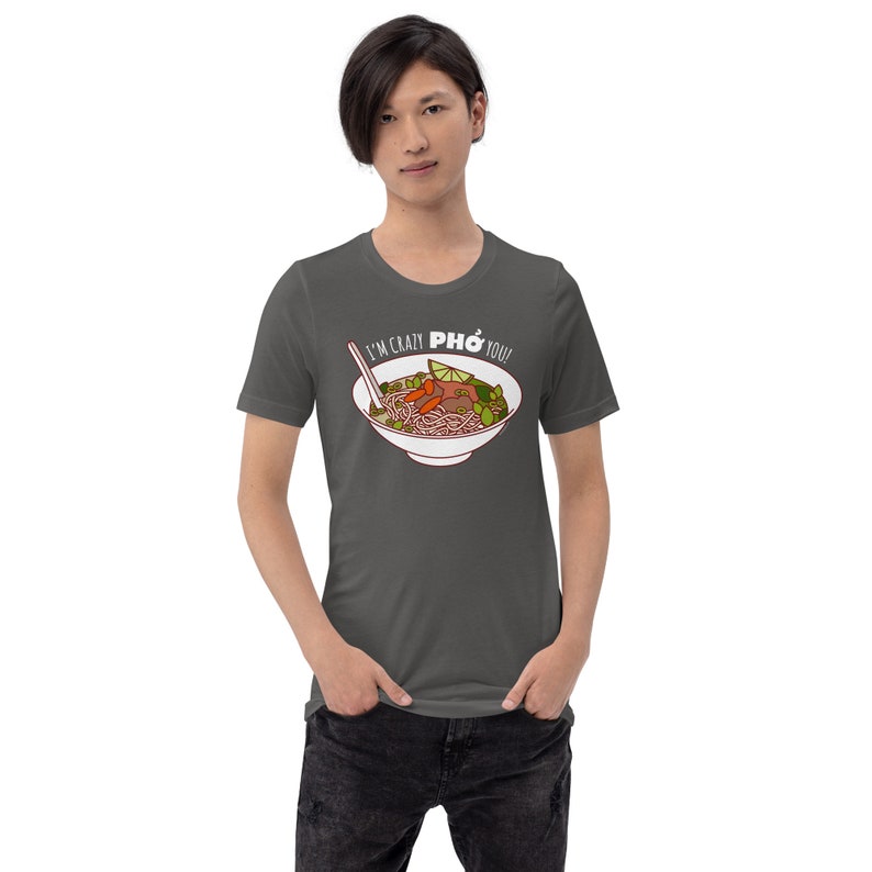 Op de afbeelding: Een donkergrijs T-shirt met een witte afbeelding van een kom pho en de tekst "I'm crazy PHO you!"