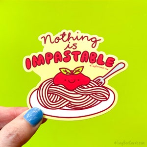 May include: A yellow sticker with a red and white illustration of spaghetti and meatballs. The text on the sticker reads "Nothing is Impastable" with a small fork and the website address "TinyBeeCards.com".