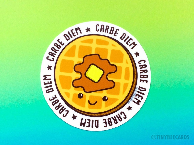 Puede incluir: Una pegatina redonda con un gofre amarillo con sirope marr&oacute;n y una porci&oacute;n de mantequilla amarilla en la parte superior. El gofre tiene una cara sonriente. La pegatina tiene el texto "Carpe Diem" repetido cuatro veces alrededor del borde.