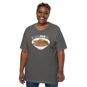Op de afbeelding: Een donkergrijs T-shirt met een witte afbeelding van een kom pho en de tekst "I'm crazy pho you!"