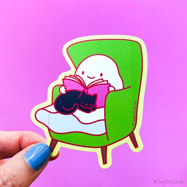 May include: A white ghost character wearing a green armchair with a black cat curled up on its lap. The ghost is reading a pink book with a red spine. The sticker is on a pink background.