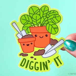 K&ouml;nnte beinhalten: Eine gr&uuml;ne Pflanze in einem Topf mit einem fr&ouml;hlichen Gesicht, ein kleinerer Topf mit einem fr&ouml;hlichen Gesicht und zwei Schaufeln. Der Text "Diggin' It" befindet sich unter den T&ouml;pfen.