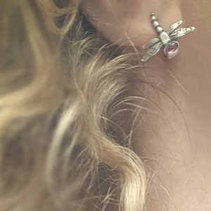 Op de afbeelding: Een zilveren ketting met een libel-hanger met een roze edelsteen. De libel is gedetailleerd met ingewikkelde vleugels en een kralenketting.