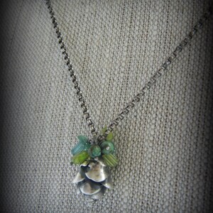 May include: A silver chain necklace with a silver pine cone pendant adorned with green and blue gemstones.