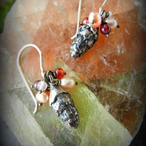 May include: A pair of silver earrings with a pine cone charm and red, pink, and white beads.