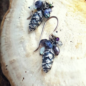May include: A pair of silver earrings with a pine cone charm and a cluster of iridescent blue, purple, and white beads.