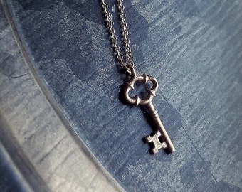May include: A silver key pendant necklace with a delicate chain. The key has an ornate design and is a popular style for jewelry.