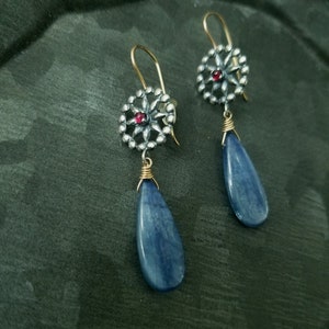 Puede incluir: Un par de pendientes de plata con una piedra azul en forma de lágrima y un dije de plata en forma de estrella con una piedra preciosa roja en el centro.