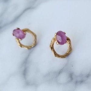 Pode incluir: Um par de brincos de ouro com uma gema oval rosa engastada em cada um. Os brincos têm um design de fio torcido.