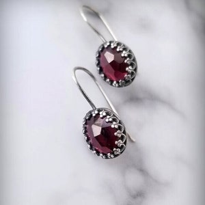 May include: A pair of silver dangle earrings with a dark red gemstone in each. The gemstones are set in a silver filigree design.