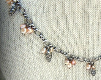 May include: A silver chain necklace with small pink pearl clusters and silver leaf charms hanging from it.