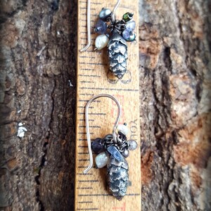 May include: A pair of silver earrings with a pine cone charm and a variety of beads, including iridescent, white, and black beads.