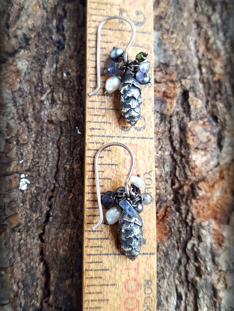 May include: A pair of silver earrings with a pine cone charm and a variety of beads, including iridescent, white, and black beads.