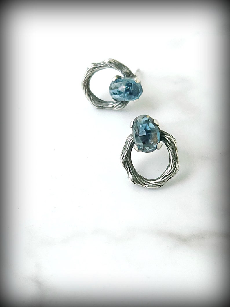 Peut inclure: Une paire de boucles d'oreilles en argent avec une pierre pr&eacute;cieuse bleue sertie dans un design de fil torsad&eacute;.