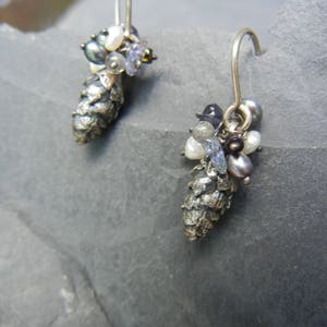 May include: A pair of silver earrings with a pine cone design. Each earring features a cluster of small, colorful gemstones and pearls.