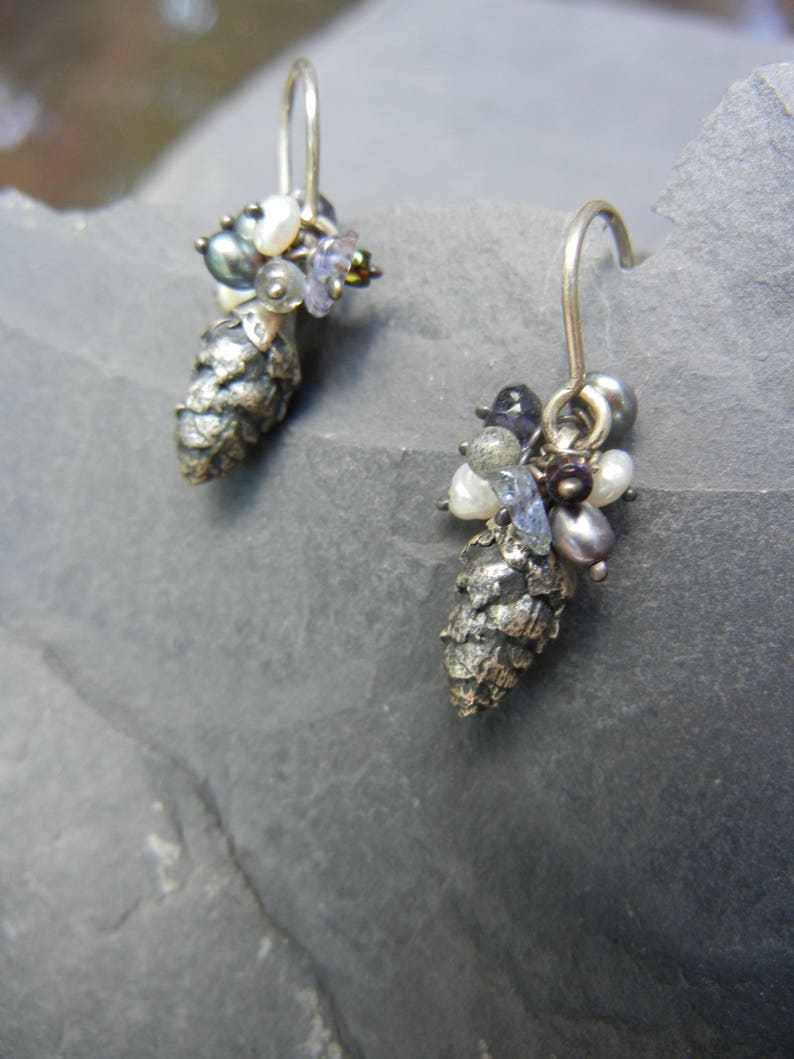 May include: A pair of silver earrings with a pine cone design. Each earring features a cluster of small, colorful gemstones and pearls.