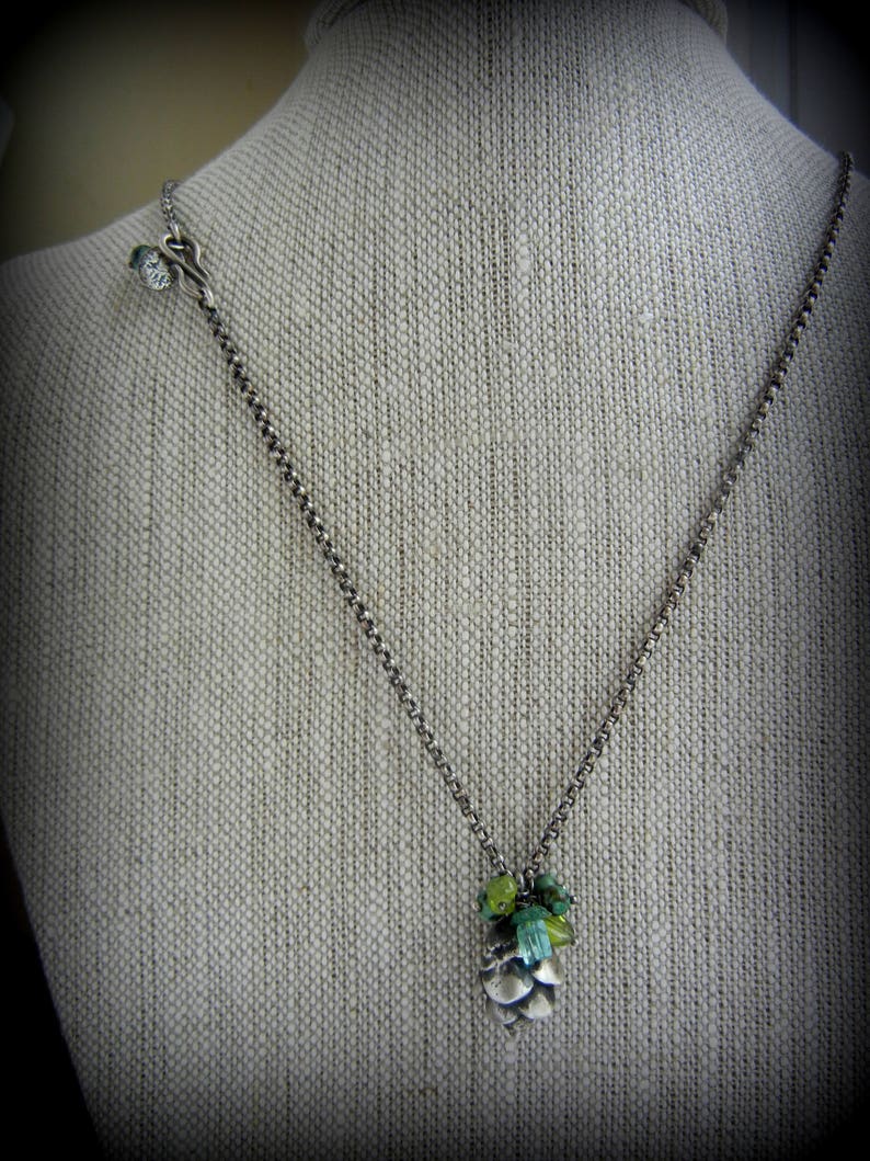 May include: A silver chain necklace with a green and blue gemstone pine cone pendant.