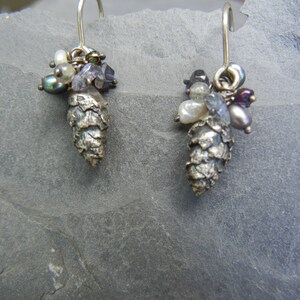 May include: A pair of silver earrings with a pine cone design. Each earring is adorned with a cluster of small, colorful beads, including white, purple, and black.