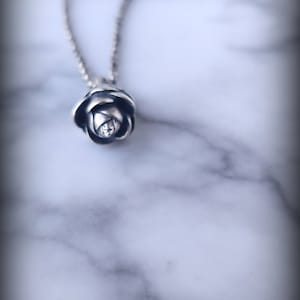 May include: A silver chain necklace with a silver rose pendant. The rose is detailed and realistic.