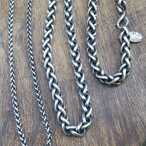 Puede incluir: Cuatro cadenas de plata de diferentes anchos y longitudes, mostradas sobre una superficie de madera. Las cadenas est&aacute;n hechas con un dise&ntilde;o trenzado.