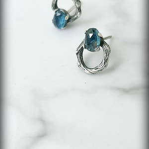 Peut inclure: Une paire de boucles d'oreilles en argent avec une pierre pr&eacute;cieuse bleue sertie dans un design en forme de brindille.