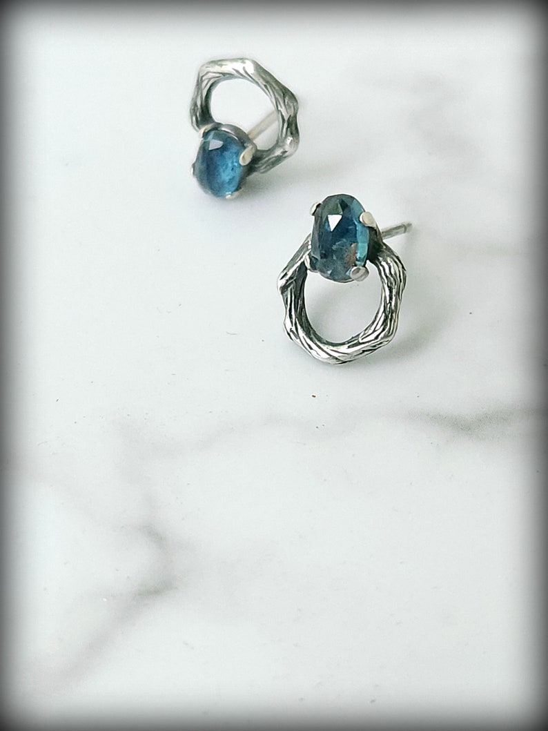 Peut inclure: Une paire de boucles d'oreilles en argent avec une pierre pr&eacute;cieuse bleue sertie dans un design en forme de brindille.
