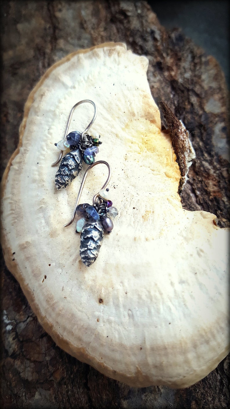 May include: A pair of silver earrings with a pine cone charm and a cluster of iridescent blue, purple, and white beads.