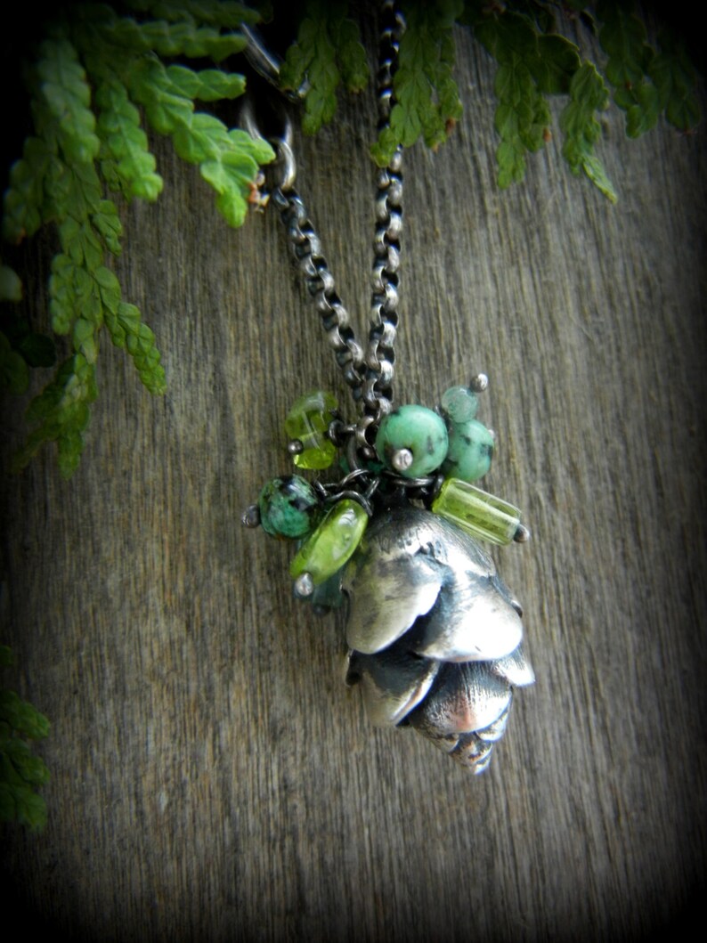 May include: A silver necklace with a pine cone pendant and green gemstone accents.