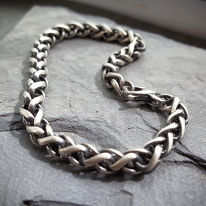 Puede incluir: Un brazalete de cadena trenzada de plata con cierre de broche.
