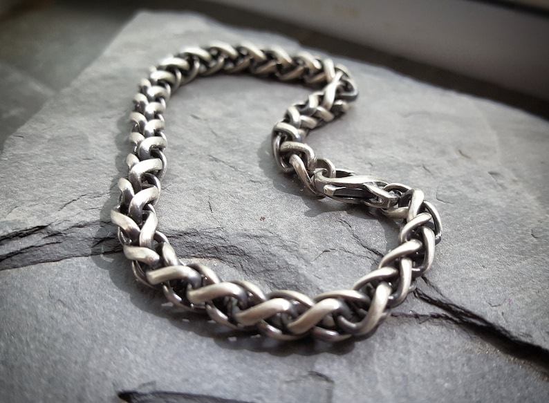 Puede incluir: Un brazalete de cadena trenzada de plata con cierre de broche.