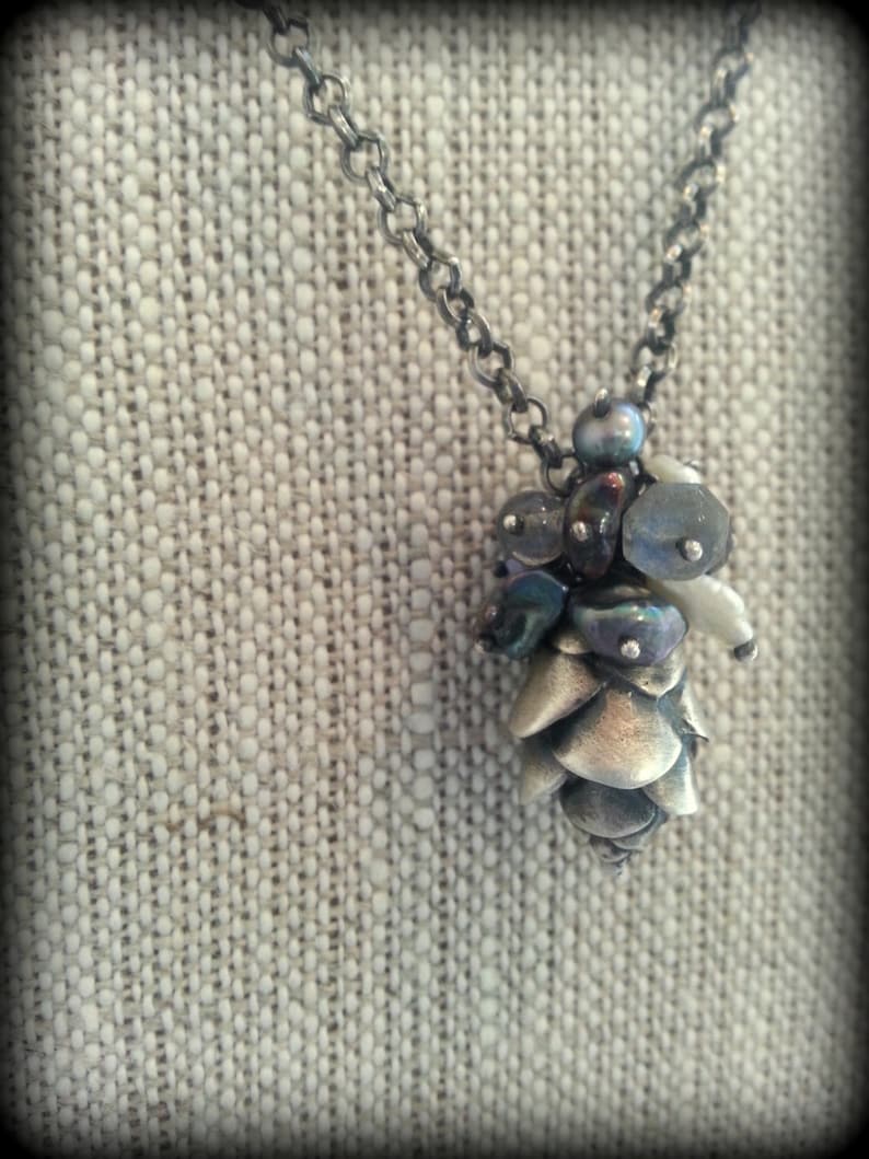 May include: A silver chain necklace with a silver and iridescent glass pine cone pendant.
